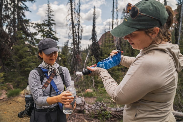 Two hikers filtering water from sawyer squeeze into a water bottle.