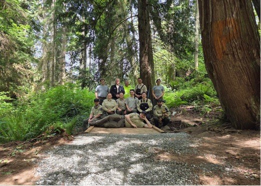 A group of park rangers sit and lay on a new bridge on a trail. 