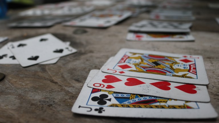 Playing cards spread out on a wooden picnic table.