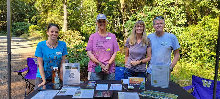Four people stand behind a table with WTA printed information.
