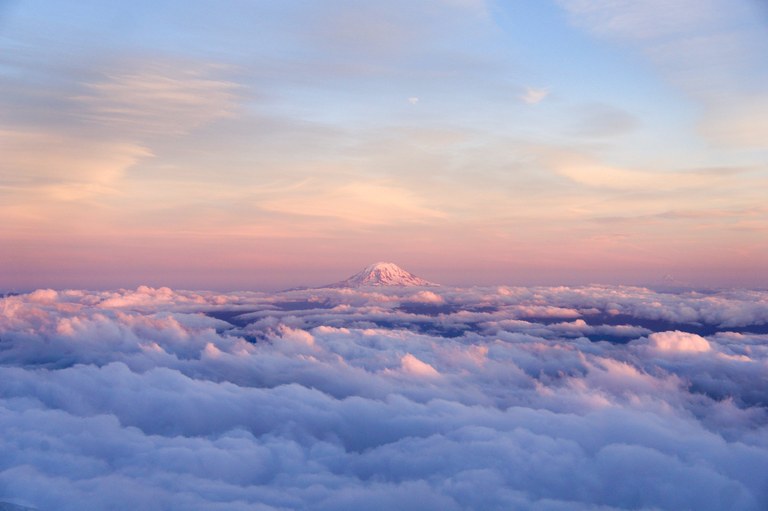 Mount Rainier rising above the clouds with pink and blue sky in the background.