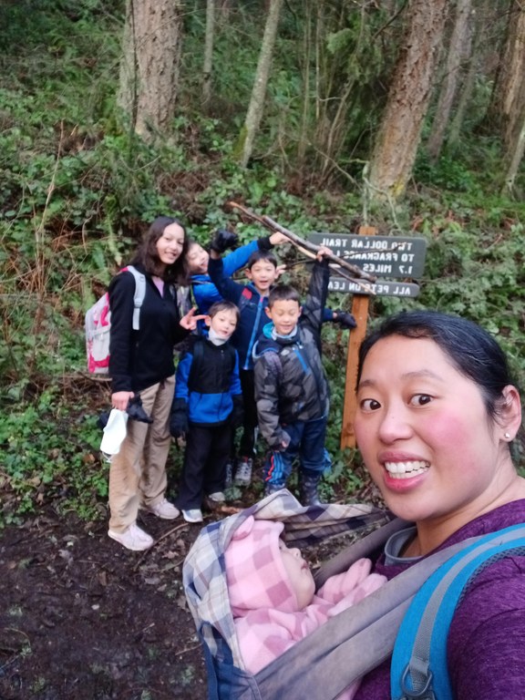 Ramfamhikes Two Dollar Trail A mom takes a selfie with a sleeping baby and five kids and a trail sign in the background.
