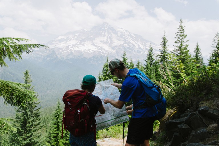 Two hikers look at a map in front of a mountain.