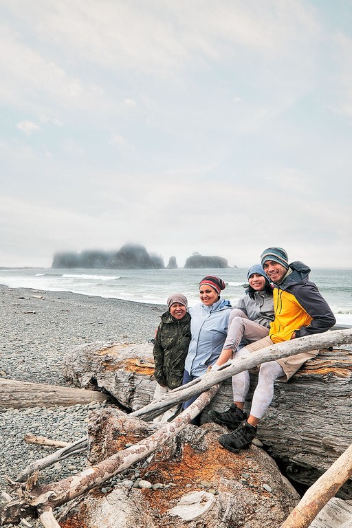A family sits on driftwood on a beach.