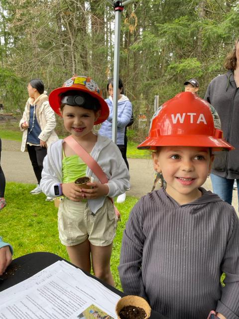 Girl in hardhat Two kids stand outside around a WTA booth outside. They are wearing orange WTA hardhats.