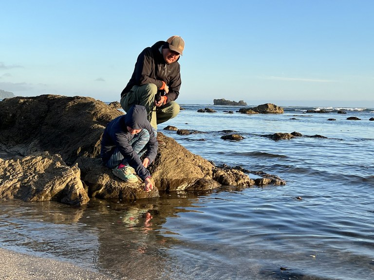 Sand Point A man and kid sit on a rock and look in the saltwater.