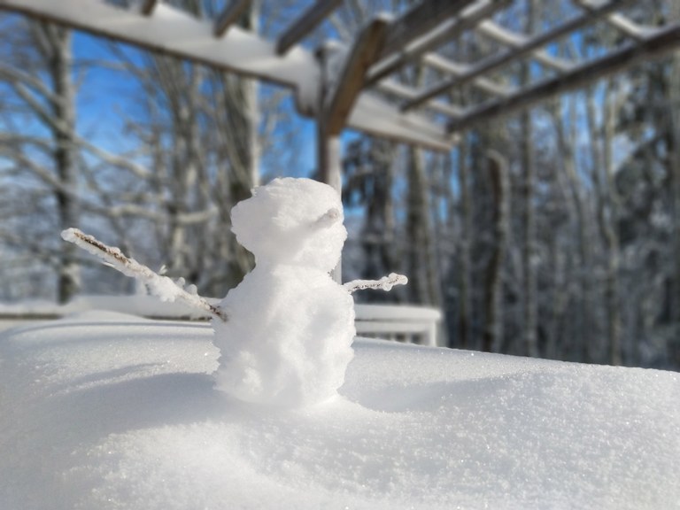 A small snowman on a snow-covered picnic table along a hiking trail.
