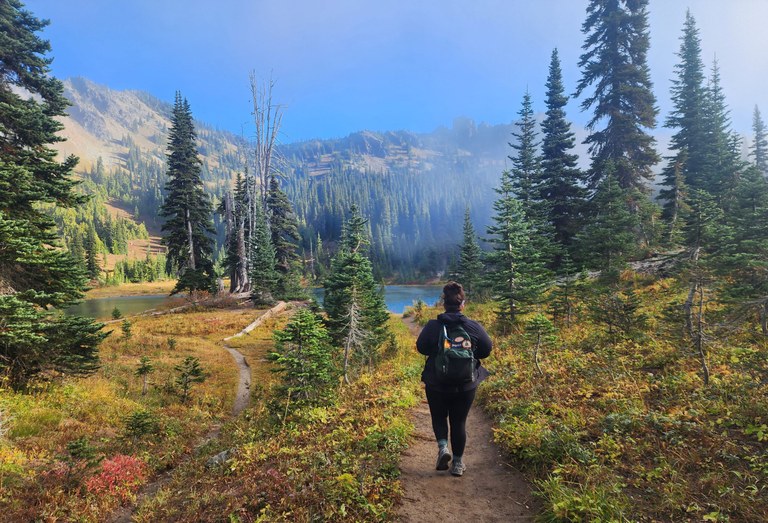 A hiker hiking toward Sheep Lake under a light layer of fog, among much fall foliage. Photo by Kyduck.