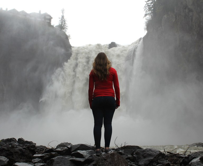 Snoqualmie Falls Megan Callahan A person wearing a bright red shirt and black leggings stands facing the massive amount of water pouring over Snoqualmie Falls.