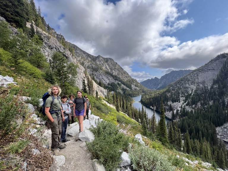 Youth volunteers smile on a trail high above a mountain lake.