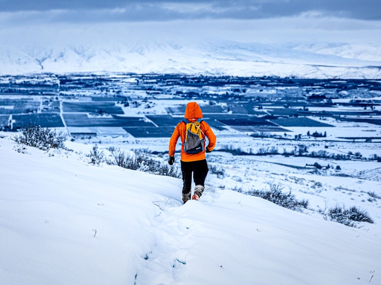 A hiker in an orange outfit walks away from the camera on a snowy hillside outside Yakima.