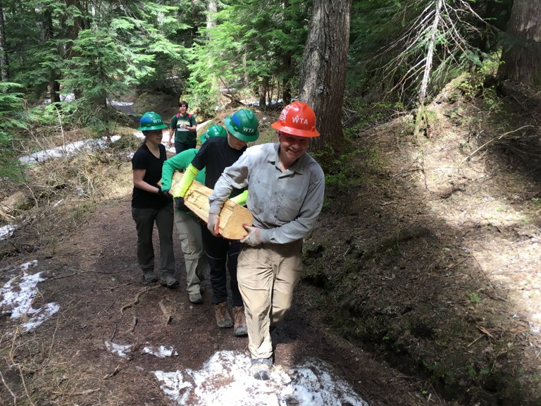 A group of volunteers carries a log across a trail with some snow on it. Photo by Hannah Tennent. 