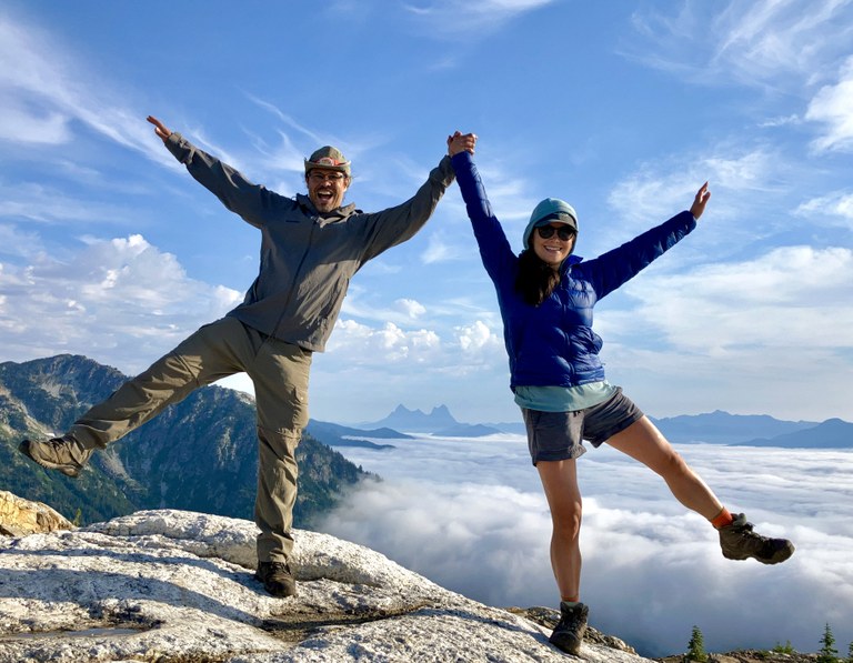 Two hikers clasp hands in celebration on top of a mountain look-out.
