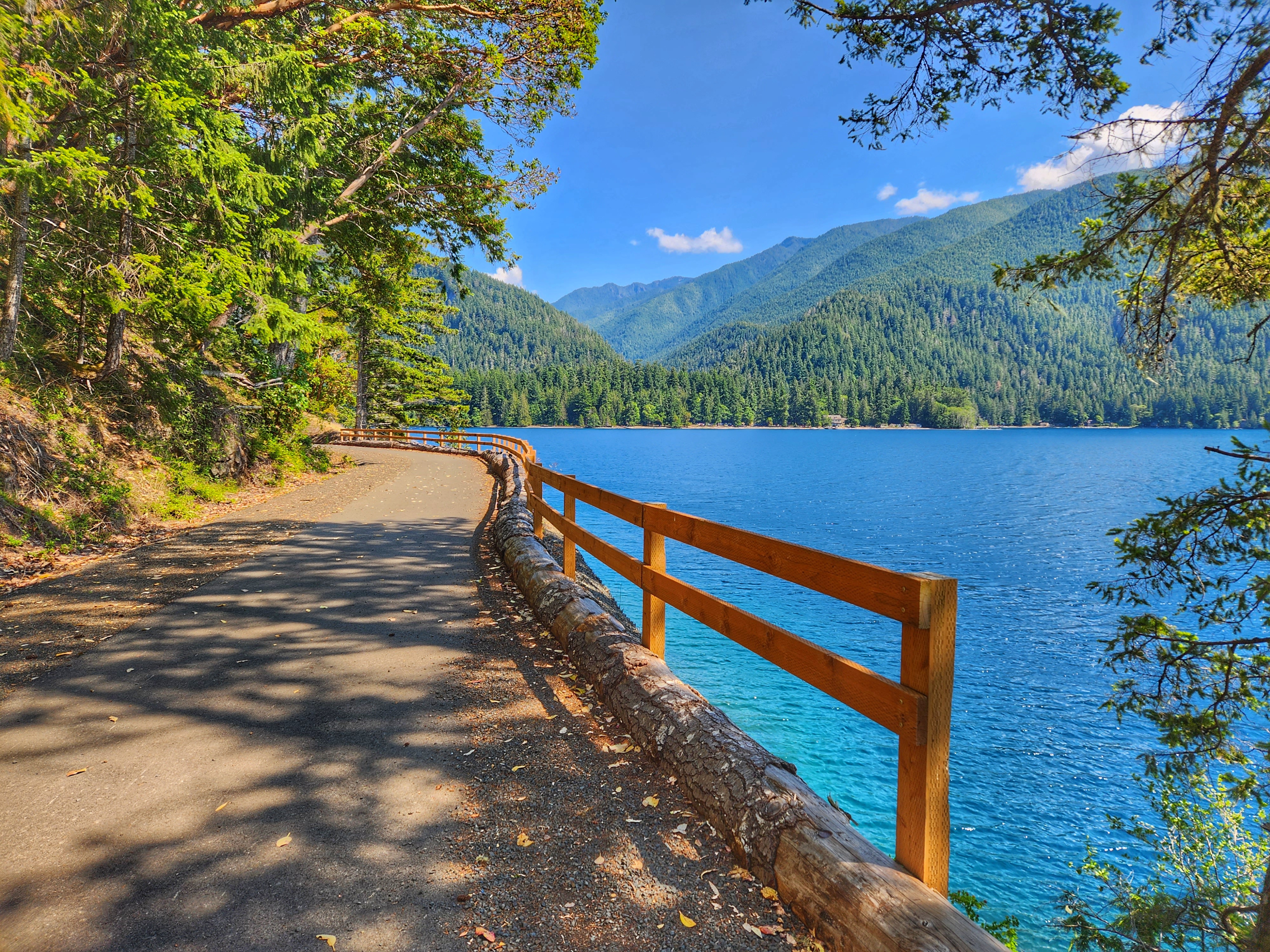 Spruce Railroad Trail by Valerie Martinson A wide, flat trail hugs the side of a blue lake on a sunny day