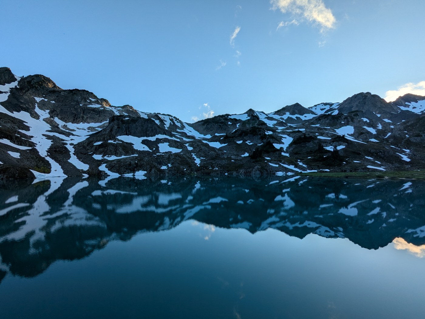 Black peaks speckled with white snow are perfectly reflected in a still lake