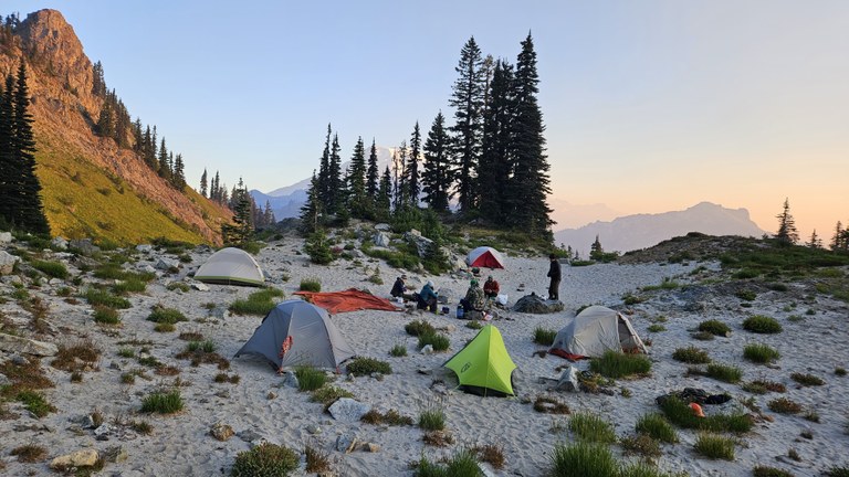 A ring of tents sit in a circle of sand on a ridgeline at sunset. 