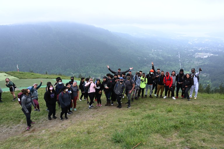 A large group of hikers smile at the camera at the summit of their hike.