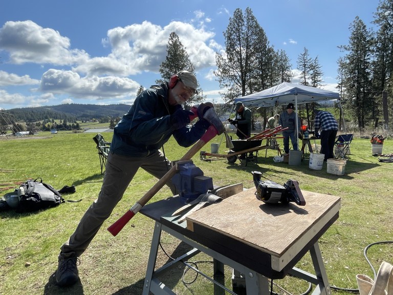 A volunteer uses a grinder to sharpen a pulaski. 