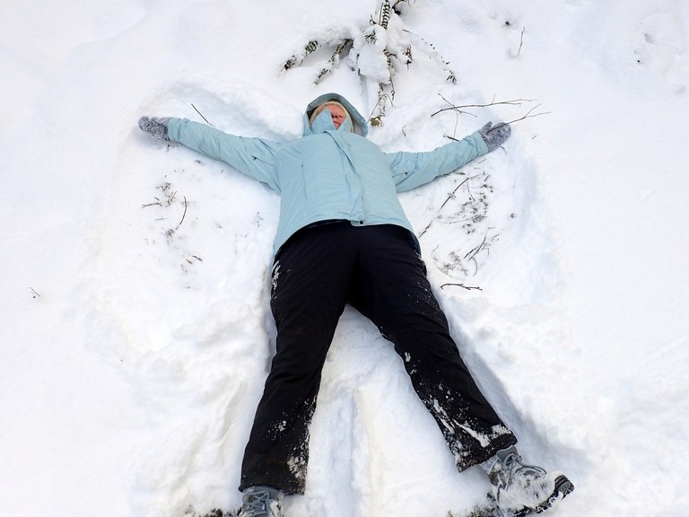 A person lays in the snow making a snow angel.
