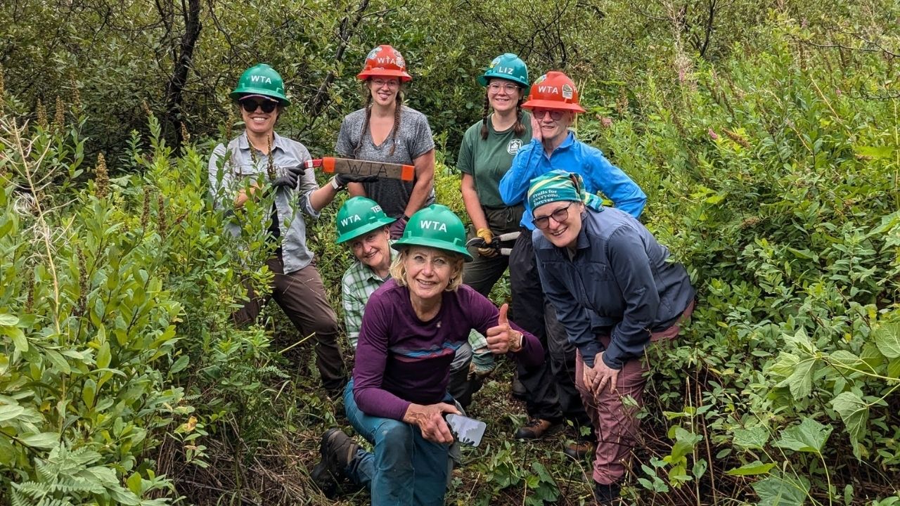 Trail crews at White River. Photo by Erin McMillan. Seven people smile at camera. Some wearing orange and green hard hats.