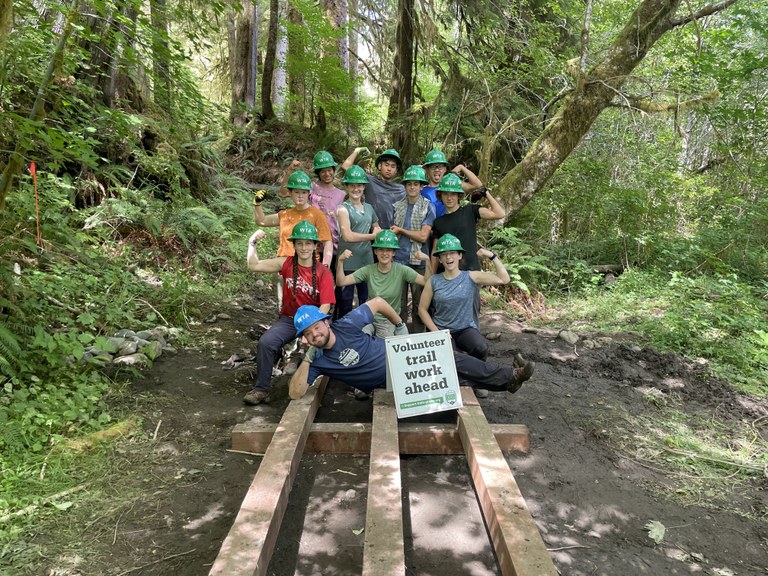 A group of teens flex their arms for a photo on a trail structure.