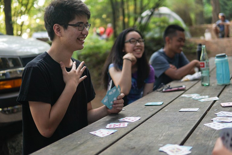 3 smiling teens enjoy a game of cards in camp on their Youth Volunteer Vacation at Moran State Park. Photo by Britt Lê