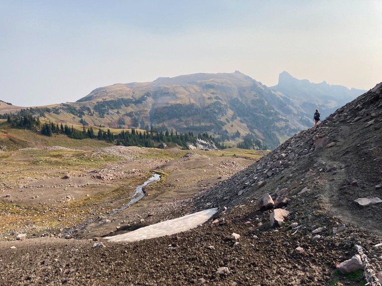 A hiker alone on a stark landscape full of rocks and dramatic peaks. 