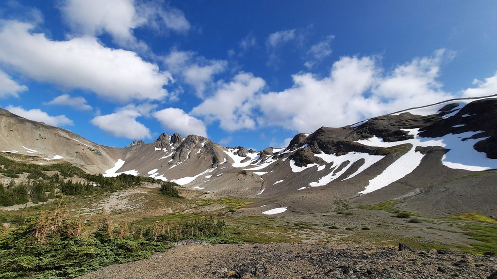 A long horizon dominated by two sloping hillsides coming together at a low point. In the foreground is a grassy meadow with a trail in the center.