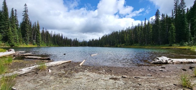 A shimmering lake set in a brown bowl at the base of a hillside with a blue and cloudy sky in the background