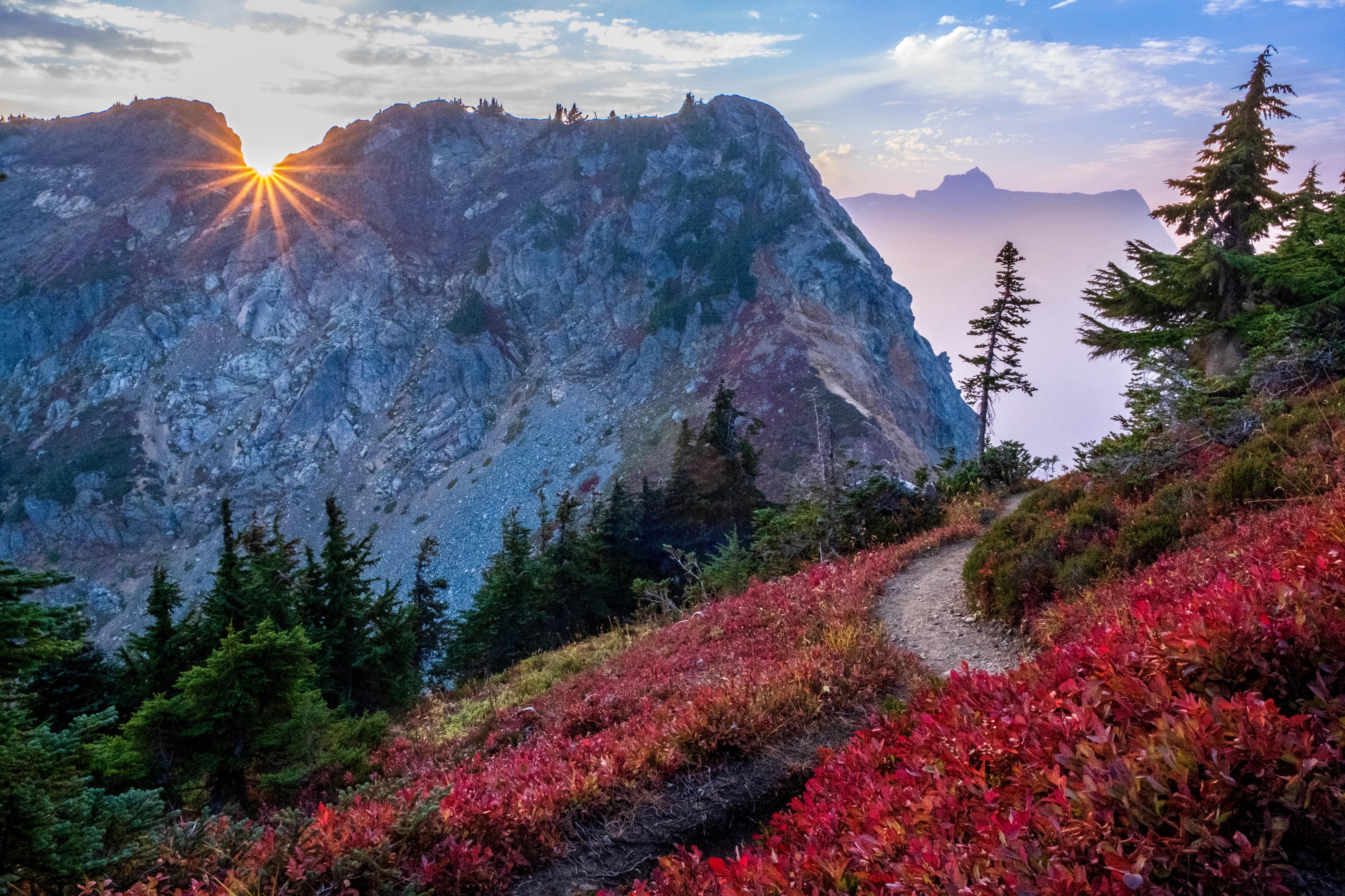 Winchester Mountain by Michael Freedman Golden sun rays peak out over a mountain ridge while a trail winds through vegetation turned red for the autumn